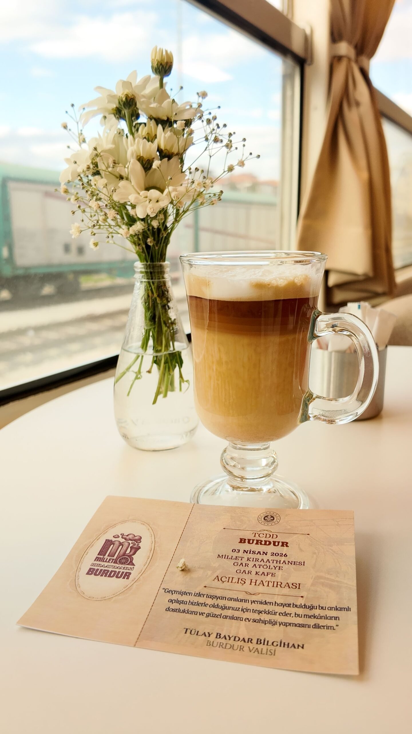 Elegant cafe scene with cappuccino and flowers by the window in Burdur, Türkiye.